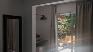 Un dormitorio con cama, espejo, una mesita y vistas a un espacio exterior con plantas y un banco.