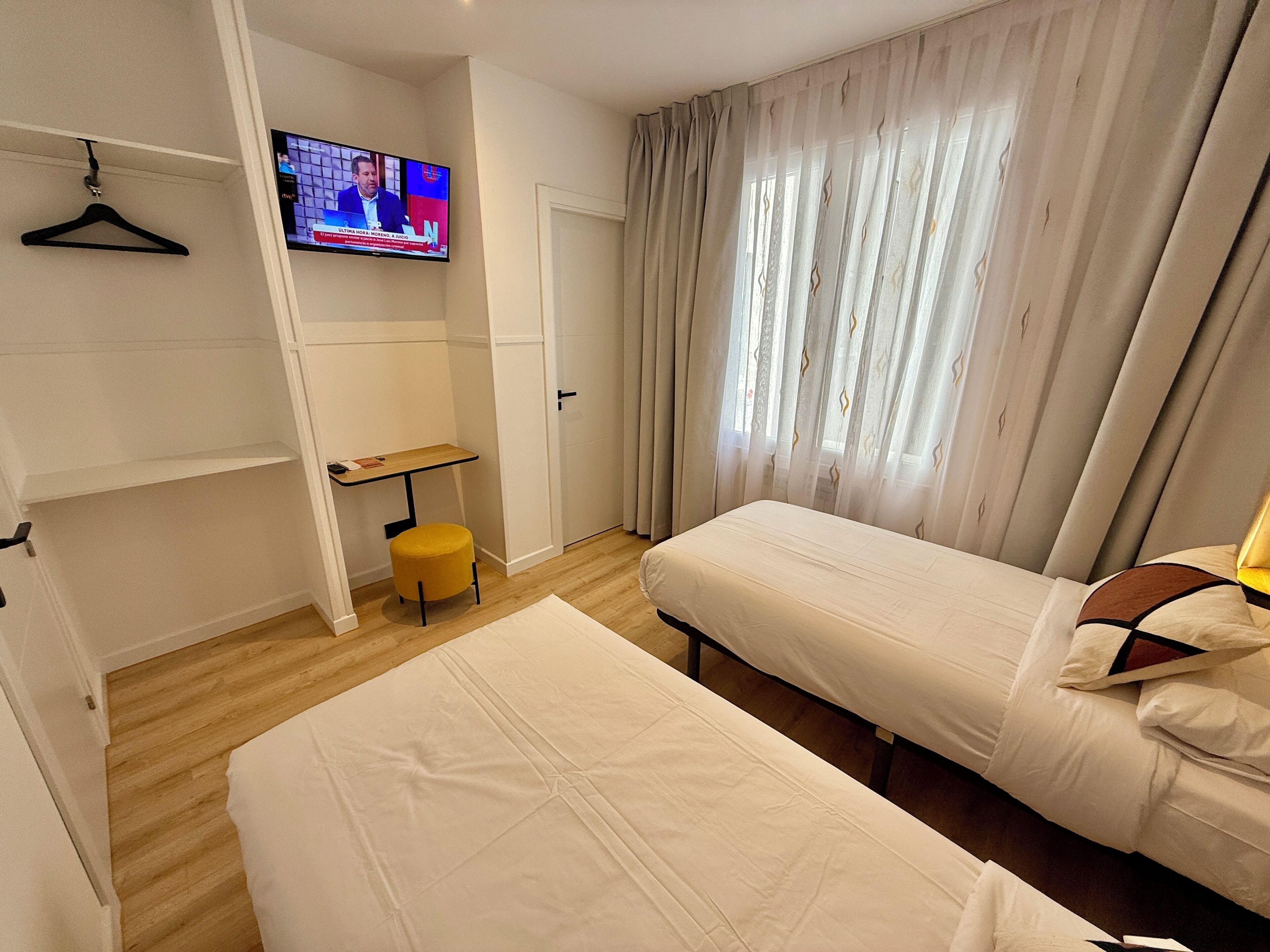 Una habitación de hotel con cama, una mesita, una silla, televisión y armario.
