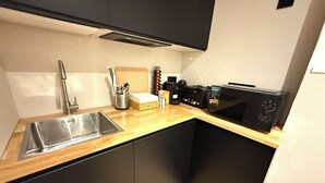 A compact kitchen with a sink, black cabinets, a wooden countertop, and a black microwave.