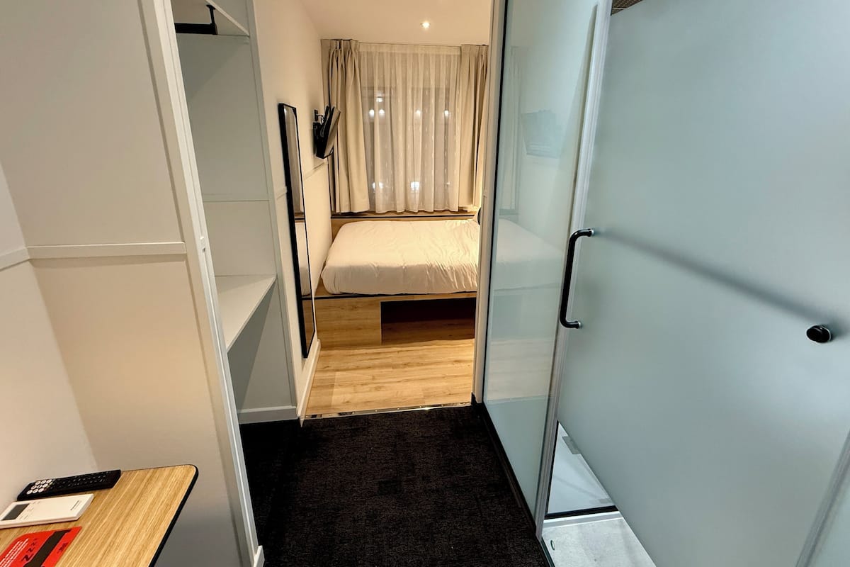 A compact hotel room with a bed, a desk, and a wardrobe.