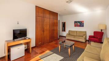 Uma sala de estar com televisão, sofá, poltrona vermelha, mesa de centro de vidro e armário de madeira.