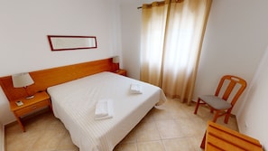 A hotel room with a bed, a nightstand, a chair, a lamp, and a window with curtains.