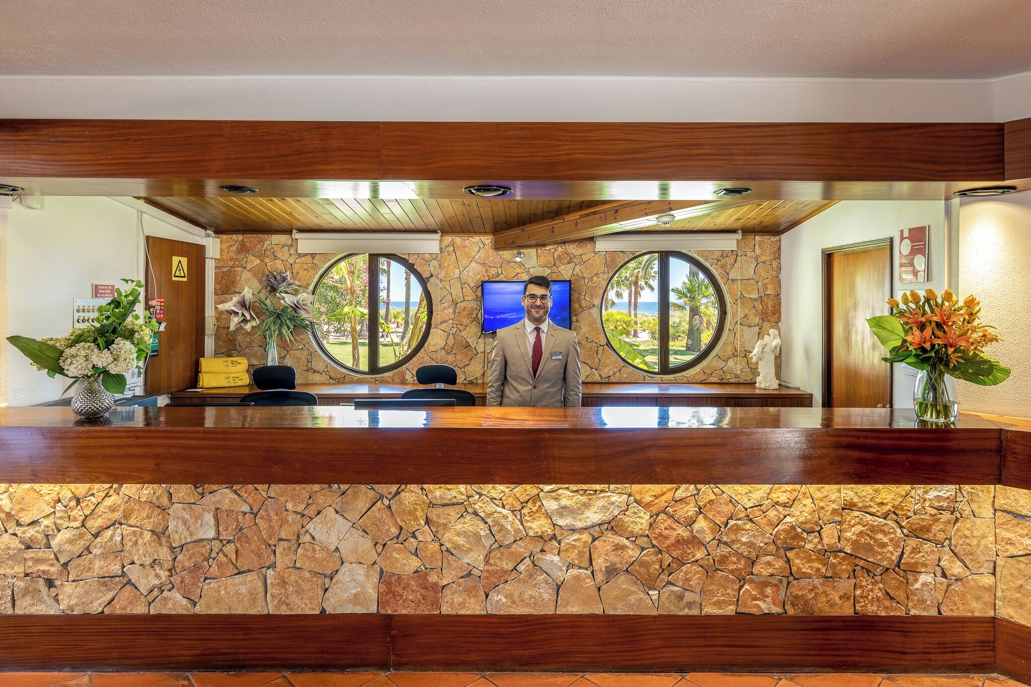 Un mostrador de recepción con fachada de piedra, paneles de madera y una pantalla de televisión.