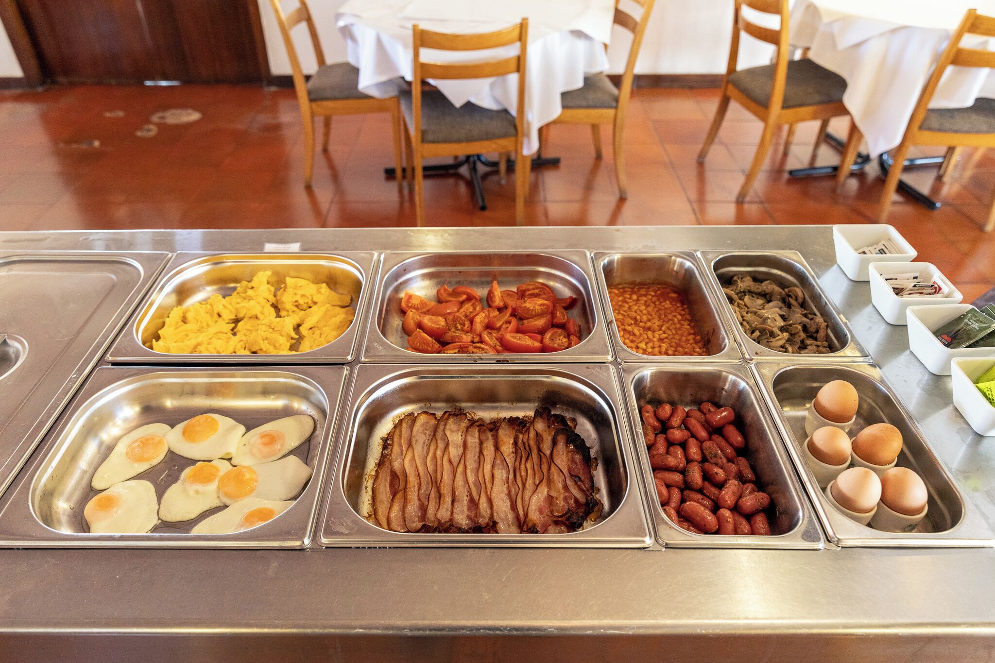 A buffet with various food options including eggs, bacon, beans, and other dishes.