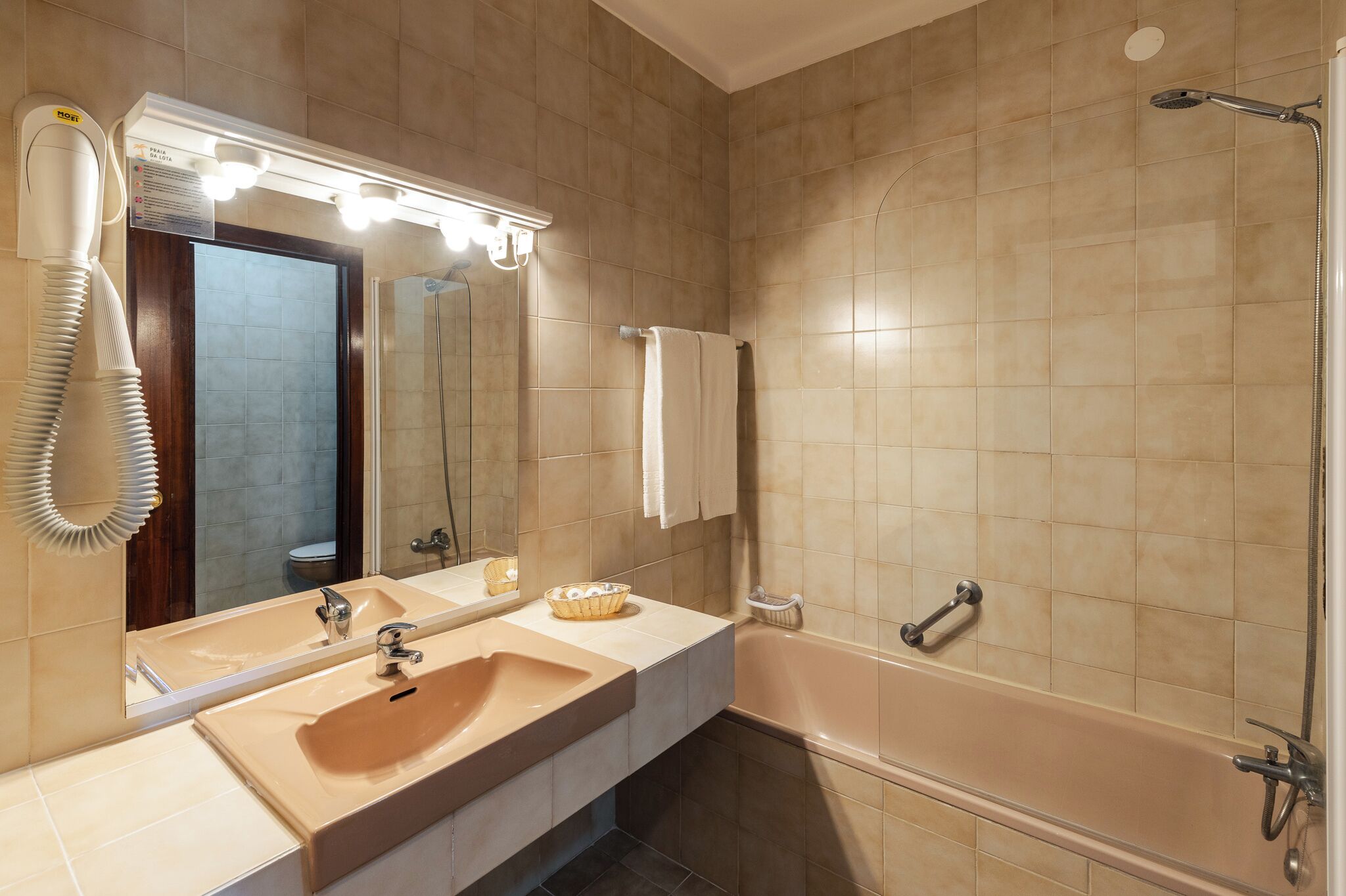 A bathroom with a double sink, a large mirror, a hairdryer, a shower, and a towel rack.