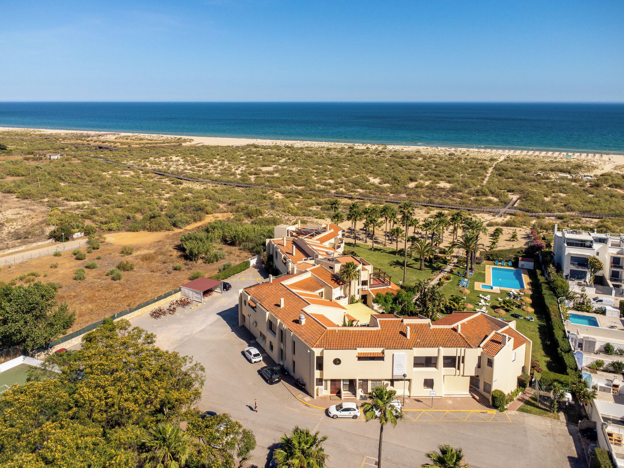 A coastal hotel with multiple buildings, a swimming pool, and a view of the beach and ocean.