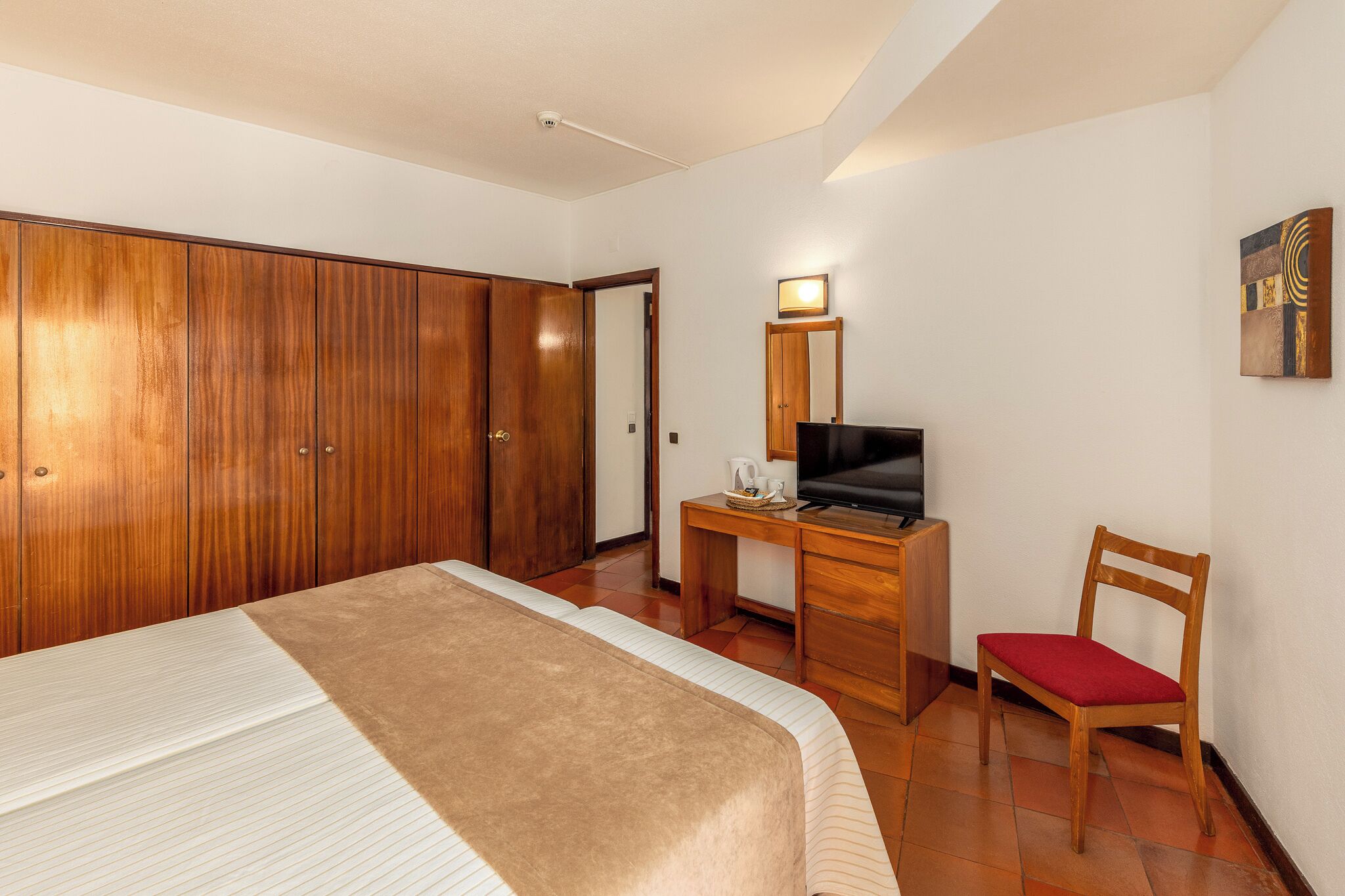 Una camera d'albergo con un letto, una scrivania con televisore, una sedia e un armadio.
