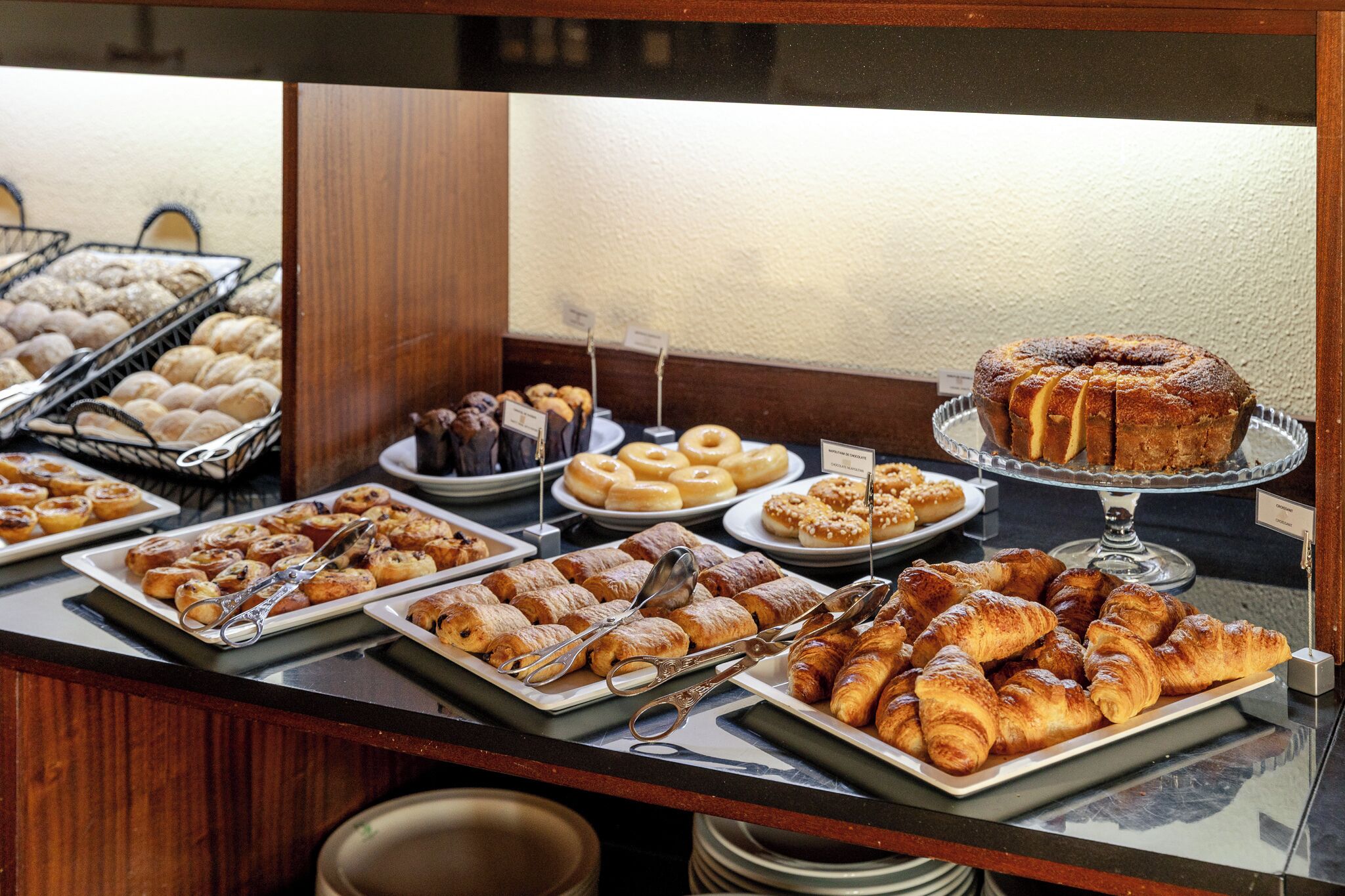 A buffet with various baked goods including pastries, croissants, and a bundt cake.