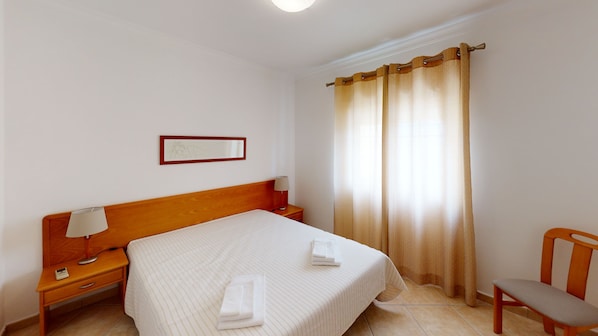 A hotel room with a wooden bed, a nightstand with a lamp, a chair, and a window with curtains.