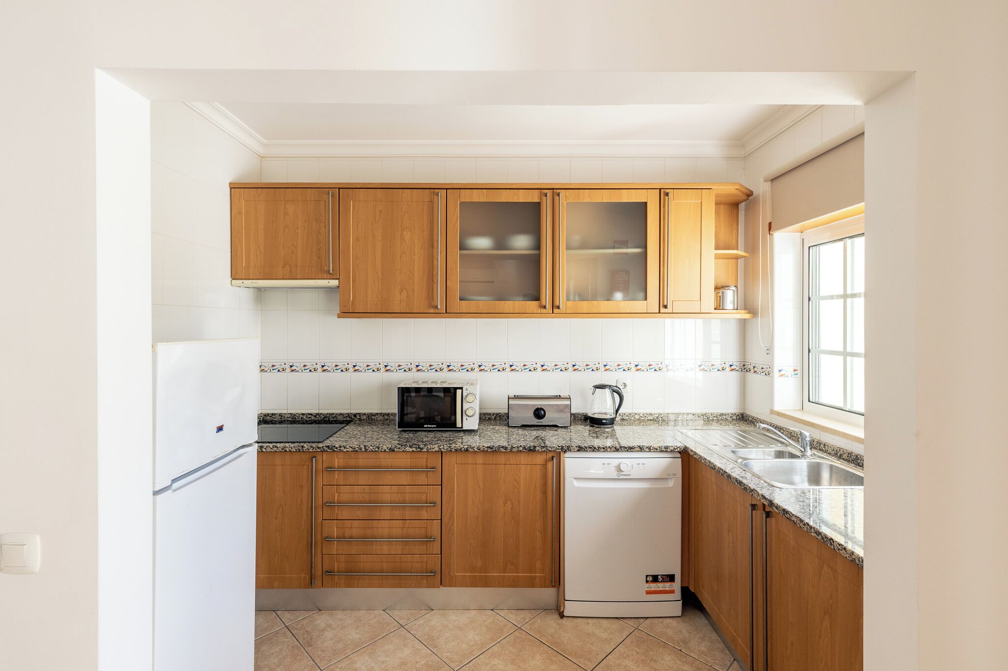 A kitchen with wooden cabinets, a microwave, a toaster, a dishwasher, and a window.