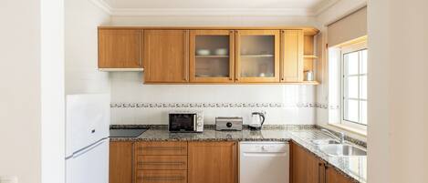 A kitchen with wooden cabinets, a microwave, a toaster, a dishwasher, and a window.