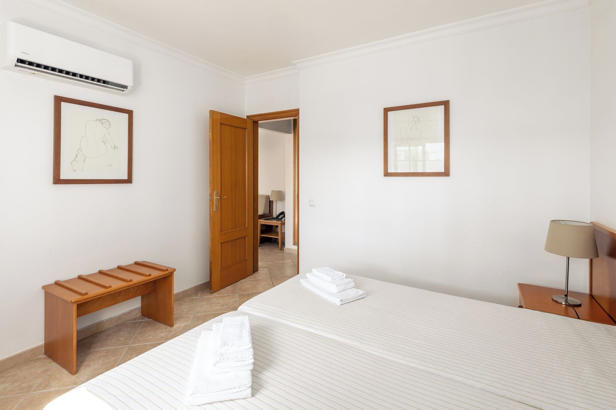 Une chambre d’hôtel avec un lit, un banc en bois, un bureau et deux tableaux encadrés accrochés aux murs.
