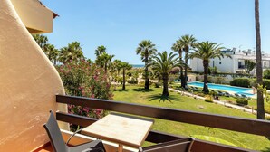 A balcony with a table and chairs, overlooking a pool and palm trees. - Praia da Lota Resort – Hotel & Apartments (Vila Real Santo Antonio)