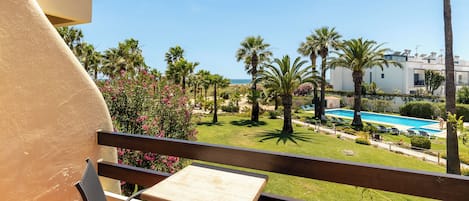 A balcony with a table and chairs, overlooking a pool and palm trees.