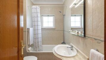 Een badkamer met een bad, wastafel, toilet, douche en een raam.