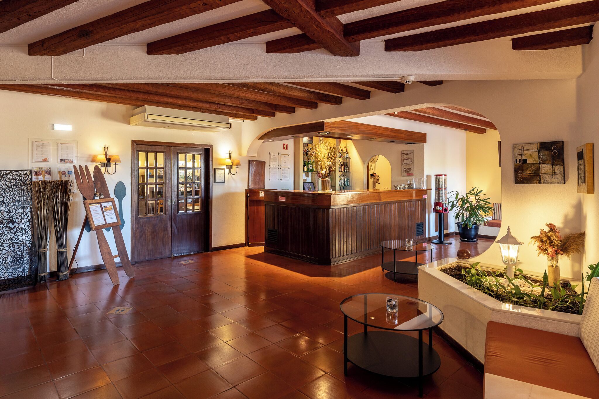 A lobby with wooden beams, a reception desk, a seating area, and a wall with framed pictures.