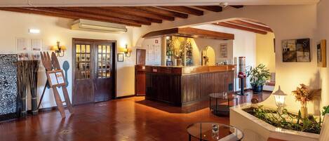 A lobby with wooden beams, a reception desk, a seating area, and a wall with framed pictures.