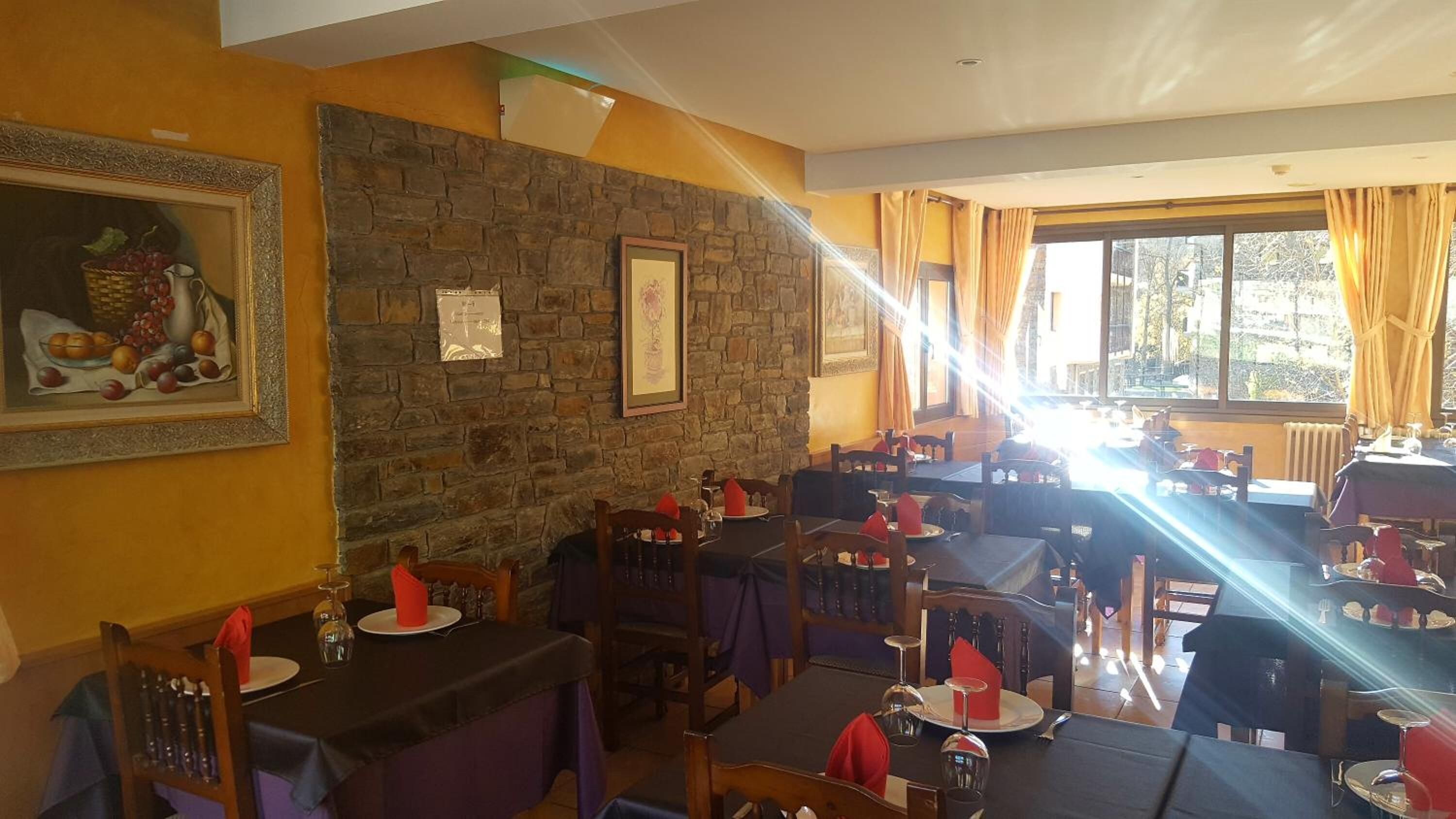 Restaurante com paredes de pedra, obras de arte emolduradas e mesas preparadas para refeições.