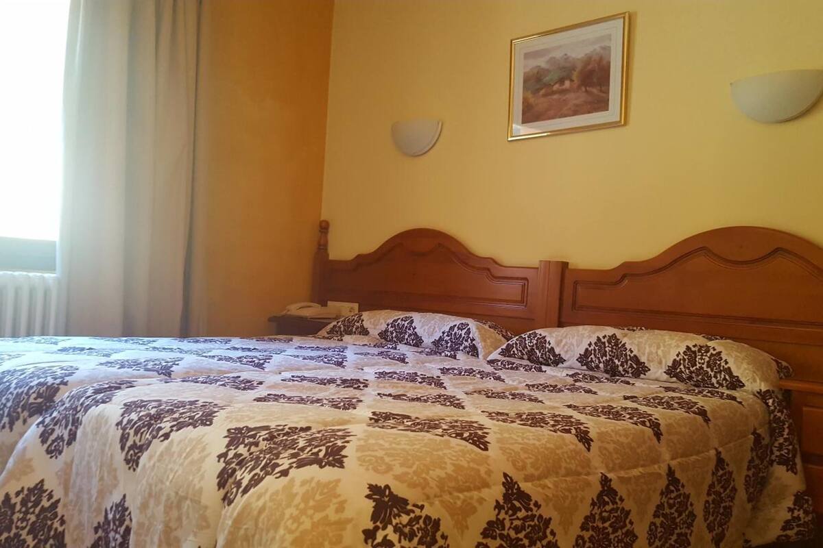 Habitación de hotel con cama doble, mesita de noche, lámpara y un cuadro en la pared.