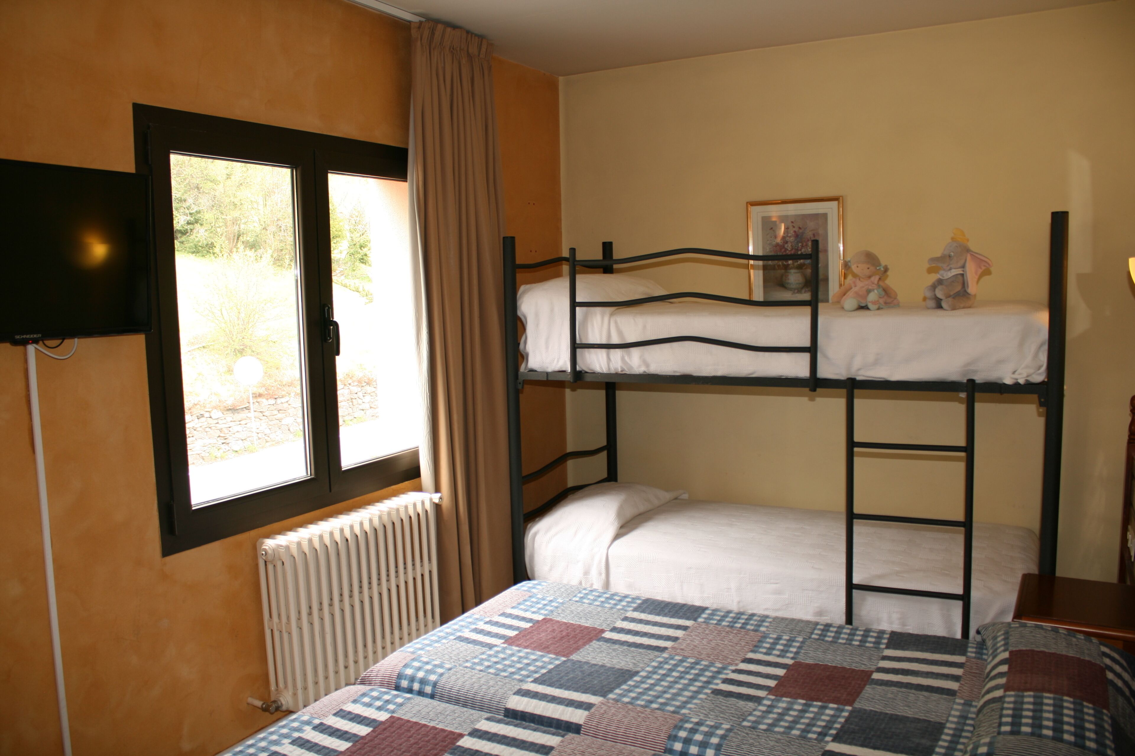 Habitación con literas, ventana, radiador y televisor.