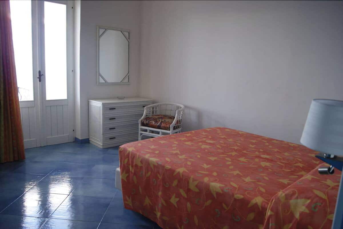A bedroom with a bed, a dresser, a chair, a mirror, and a door.