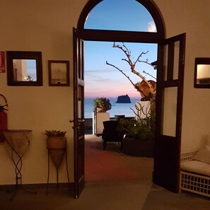 An open doorway leading to a balcony with a view of the sea and a sunset. There are potted plants and a chair on the balcony. - La Sirenetta Park Hotel (Lipari)