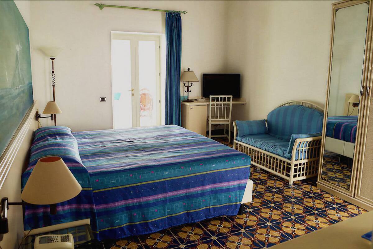 A room with a bed, a chair, a TV, and a mirror.