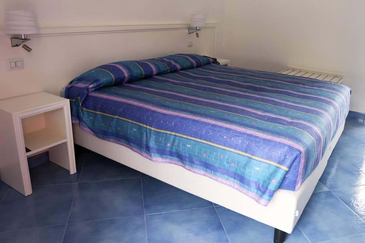 A single bed with a striped bedspread, a bedside table, and a wall-mounted lamp.