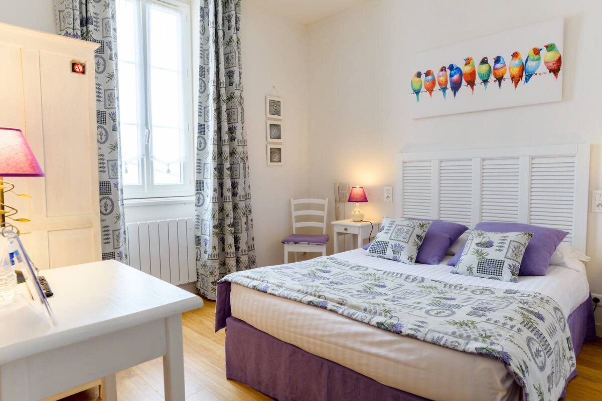 Un dormitorio con cama, escritorio, silla, radiador y ventana con cortinas.