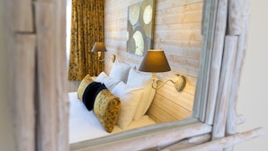 Une chambre à coucher avec une tête de lit en bois, deux lampes de chevet, un lit avec des oreillers blancs et à motifs, et une fenêtre avec des rideaux.