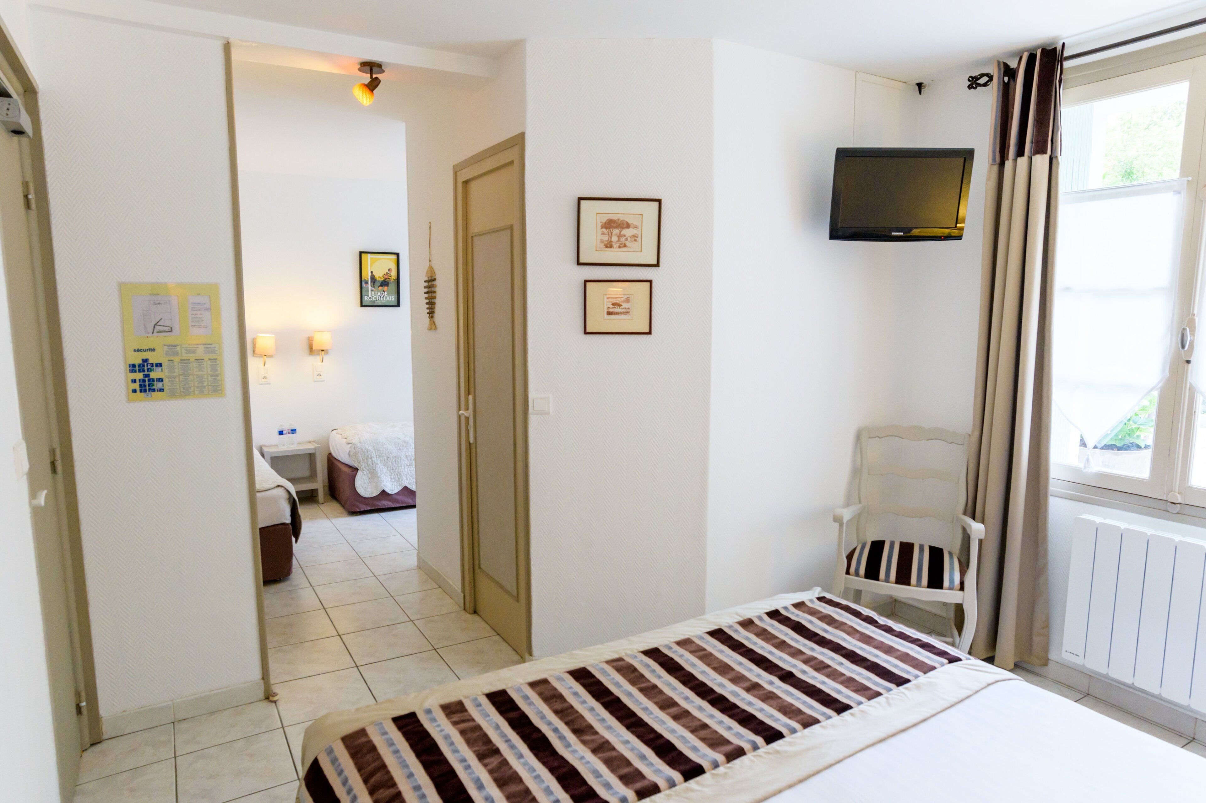Une chambre d’hôtel avec un lit, une chaise, une télévision et une fenêtre avec des rideaux.