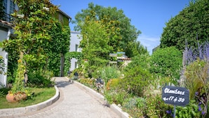 Un chemin pavé mène à un bâtiment sur lequel est apposée une enseigne indiquant « Chambres 17 à 30 ».