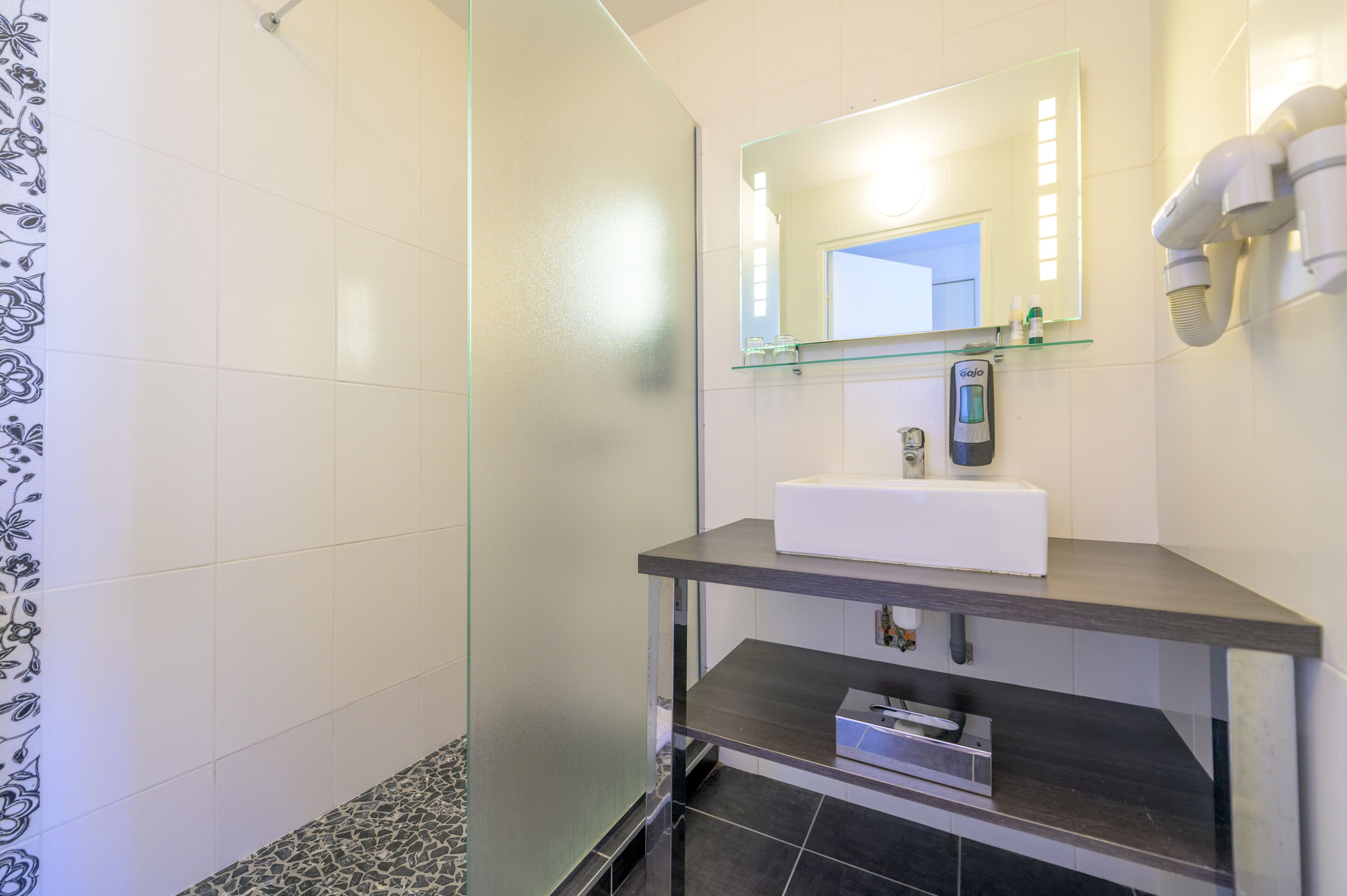 A modern bathroom with a glass shower enclosure, a white sink, and a mirror with a built-in light.