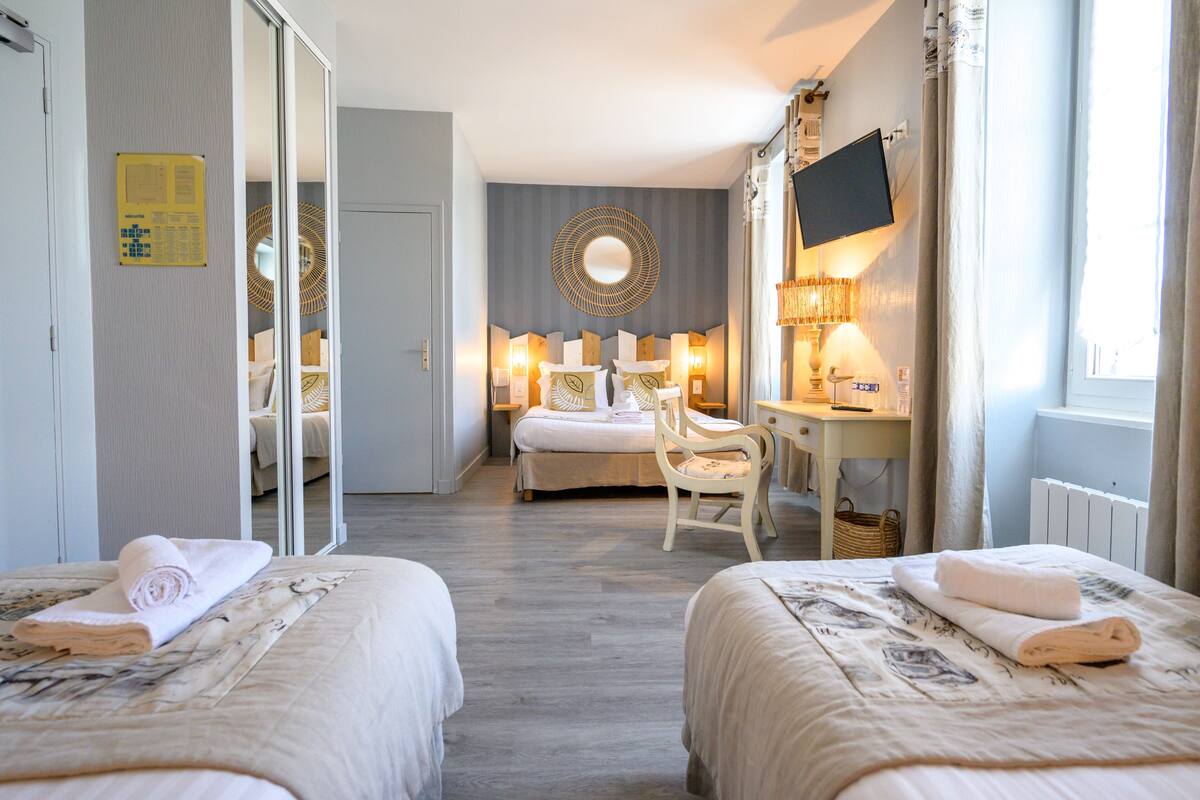 Habitación de hotel con dos camas, un escritorio, una silla, un televisor y un espejo grande.