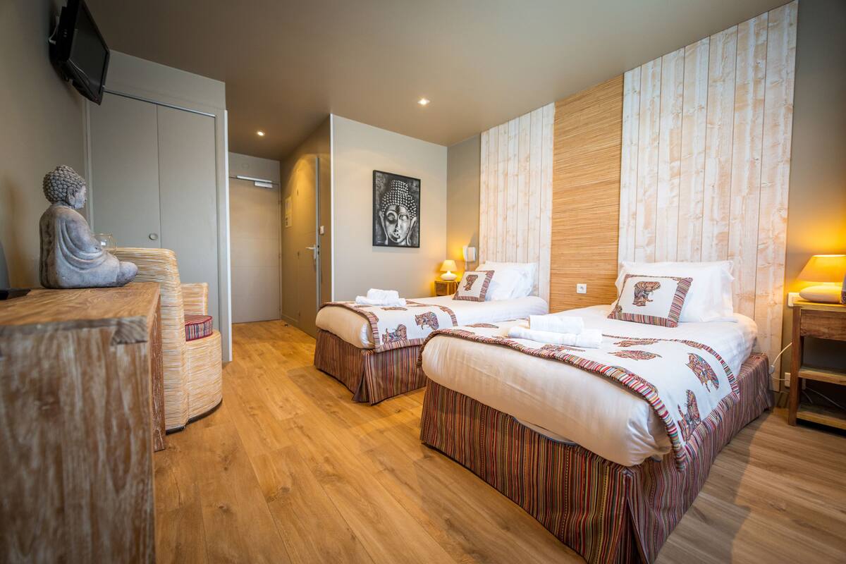 Habitación de hotel con dos camas, cabecera de madera, una estatua, televisor montado en la pared y una obra de arte enmarcada.