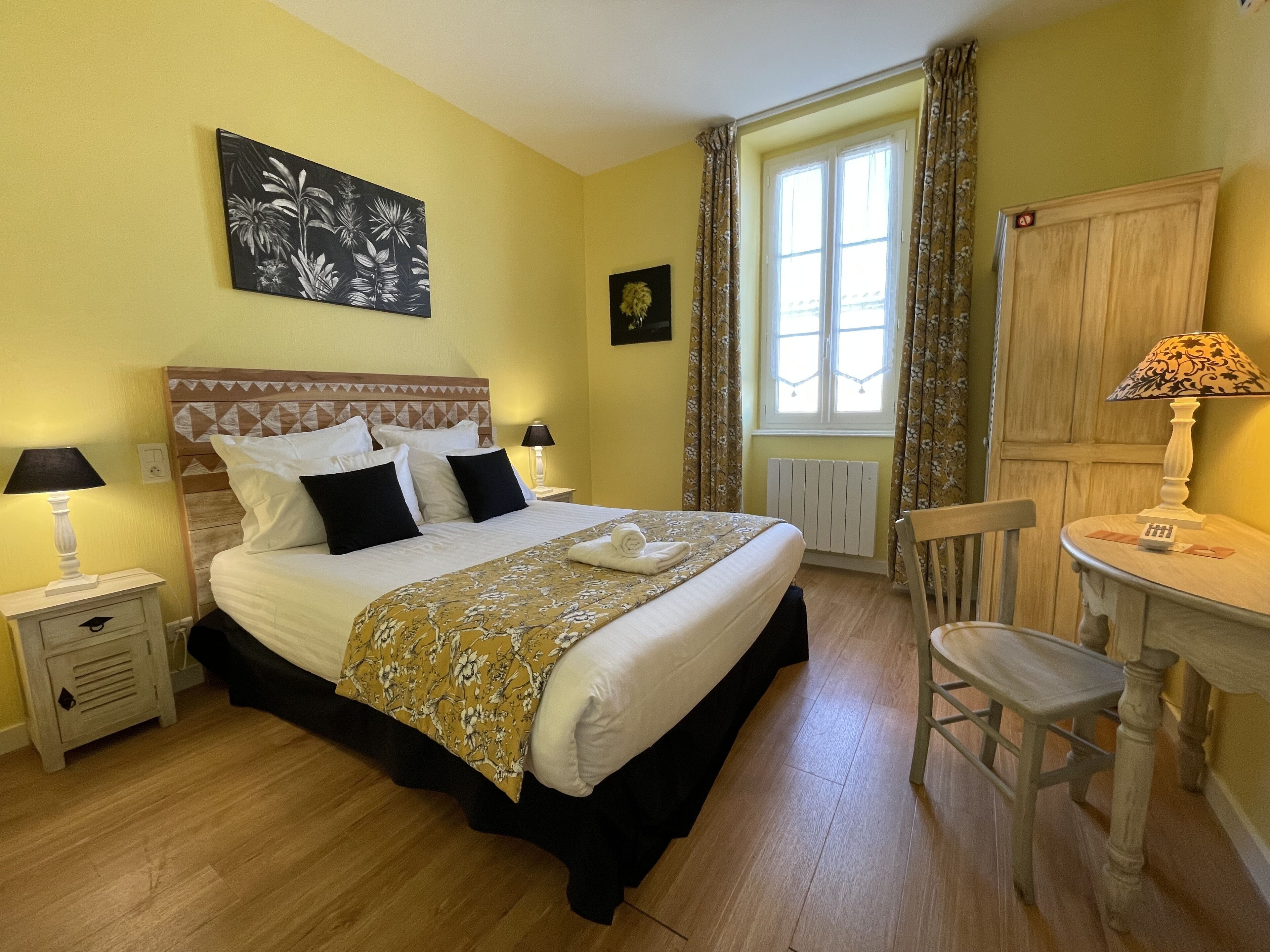 A hotel room with a bed, a chair, a table, and a window with curtains.