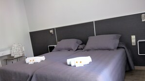 Una cama bien hecha con dos almohadas y dos toallas, una mesita de noche con lámpara, y un enchufe en la pared.