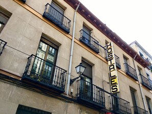 A building with multiple balconies, a sign reading "Hostales", and a window with a view of another building.