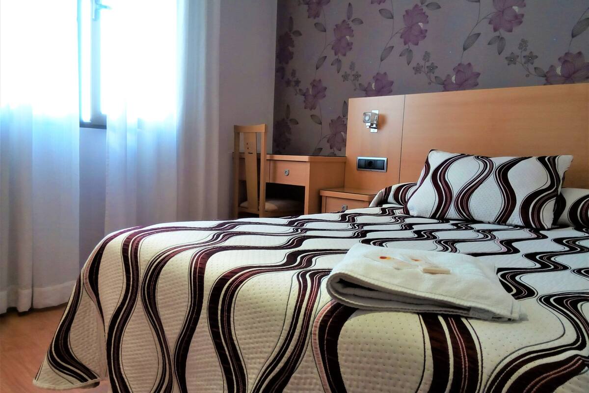 Una habitación de hotel con una cama, una mesita de noche de madera, un escritorio y una silla.