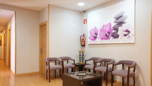 Un área de recepción con piso de madera, una mesa de centro y seis sillas moradas dispuestas alrededor. Un extintor de incendios está montado en la pared a la derecha.