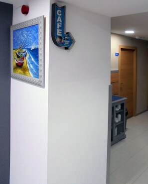 A hallway with a framed painting of boats on the wall, a sign for the cafe, and a door labeled "001". - Hostal Pensió Maricel (Sitges)