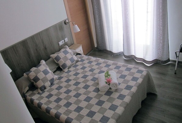 A hotel room with a checkered bedspread, two pillows, a bedside lamp, and a window with curtains.