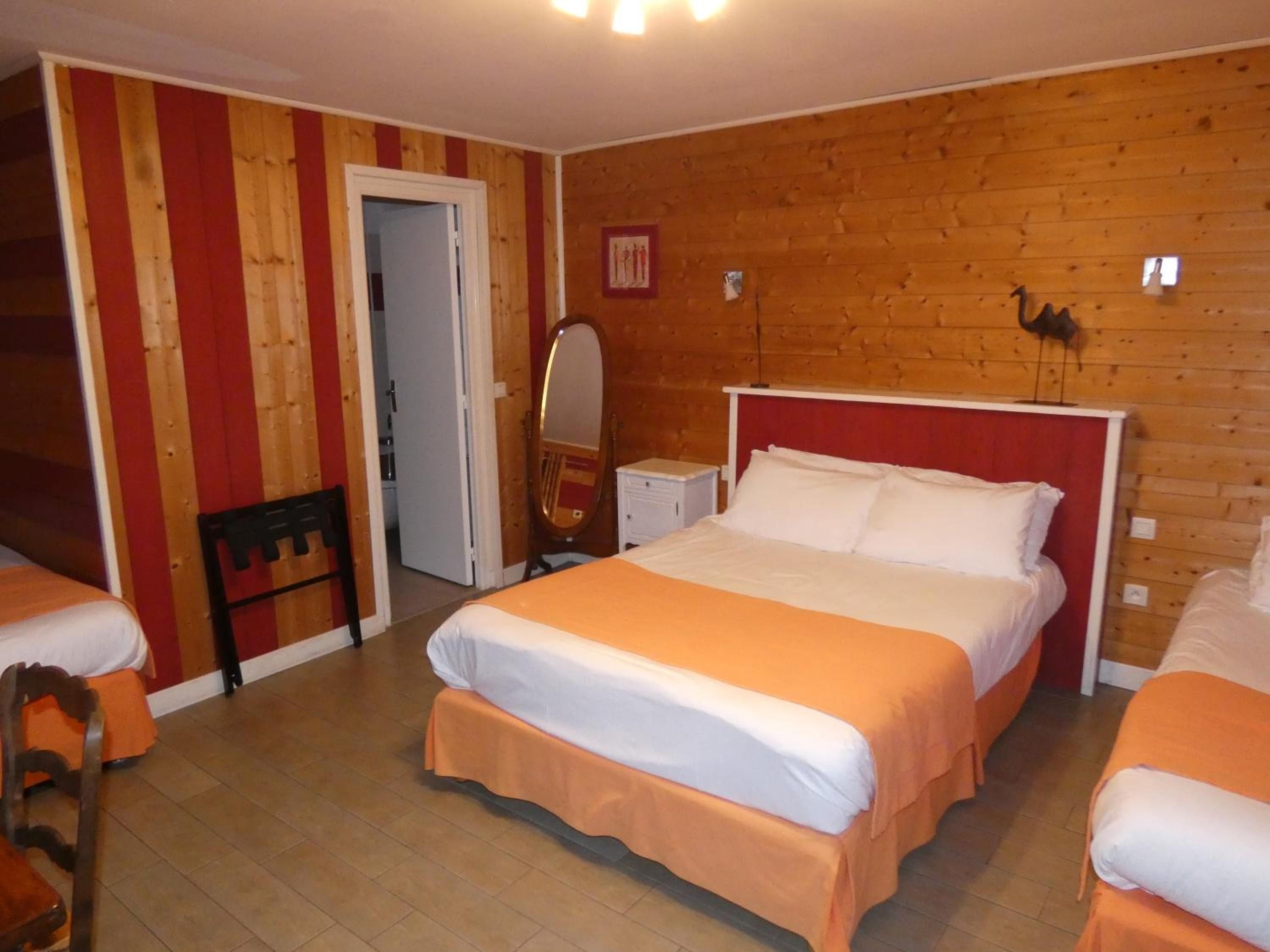 A hotel room with a wooden wall, a bed with white and orange bedding, a chair, and a small table with a mirror.