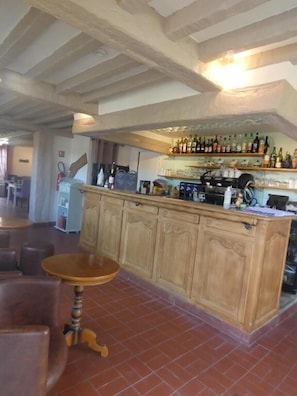 A bar area with wooden cabinets, a bar counter, and a seating area with a round table. - Auberge Saint Martin (Surville)