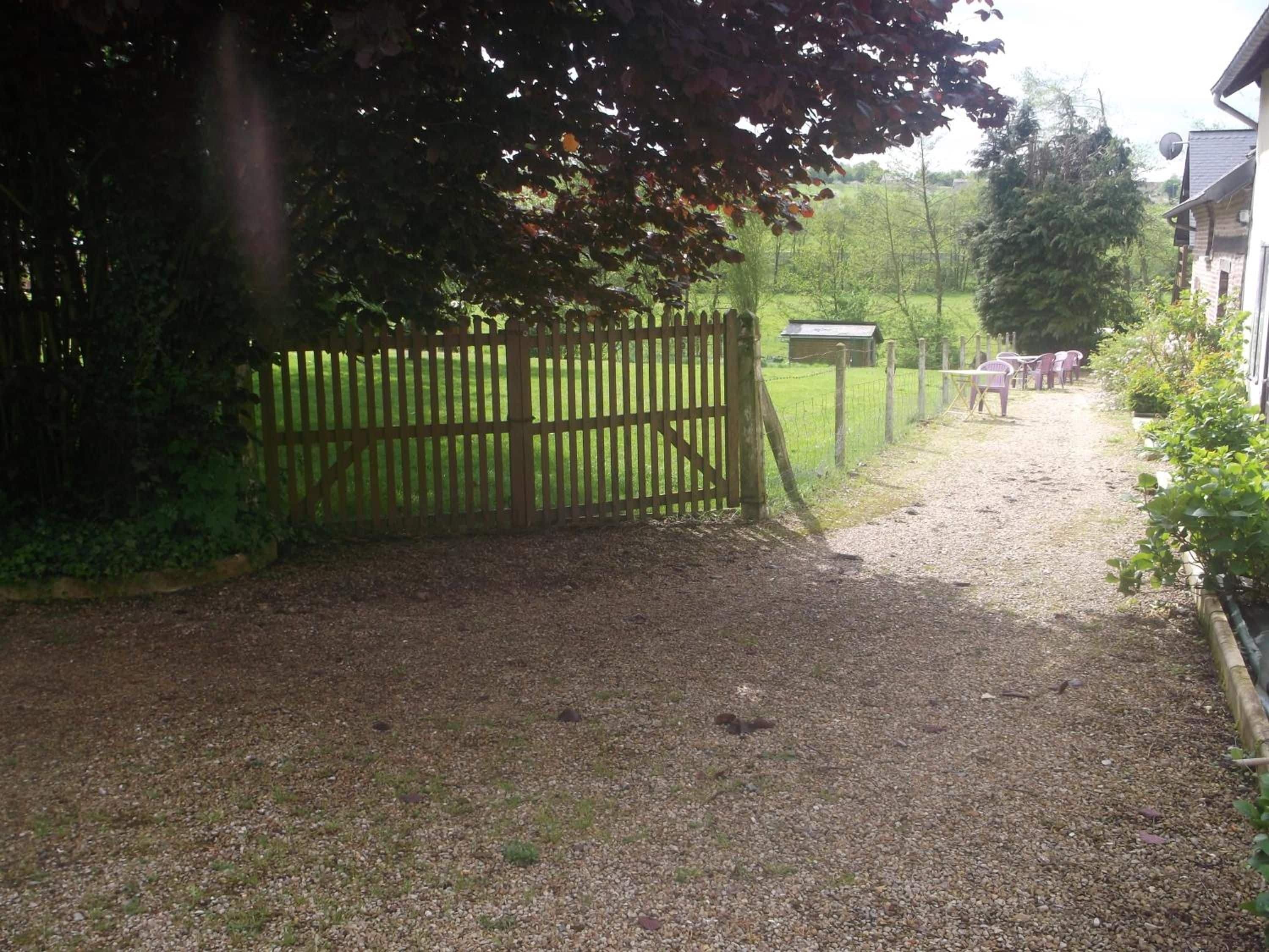A gravel driveway leading to a wooden gate, with a fenced area and a building in the background.