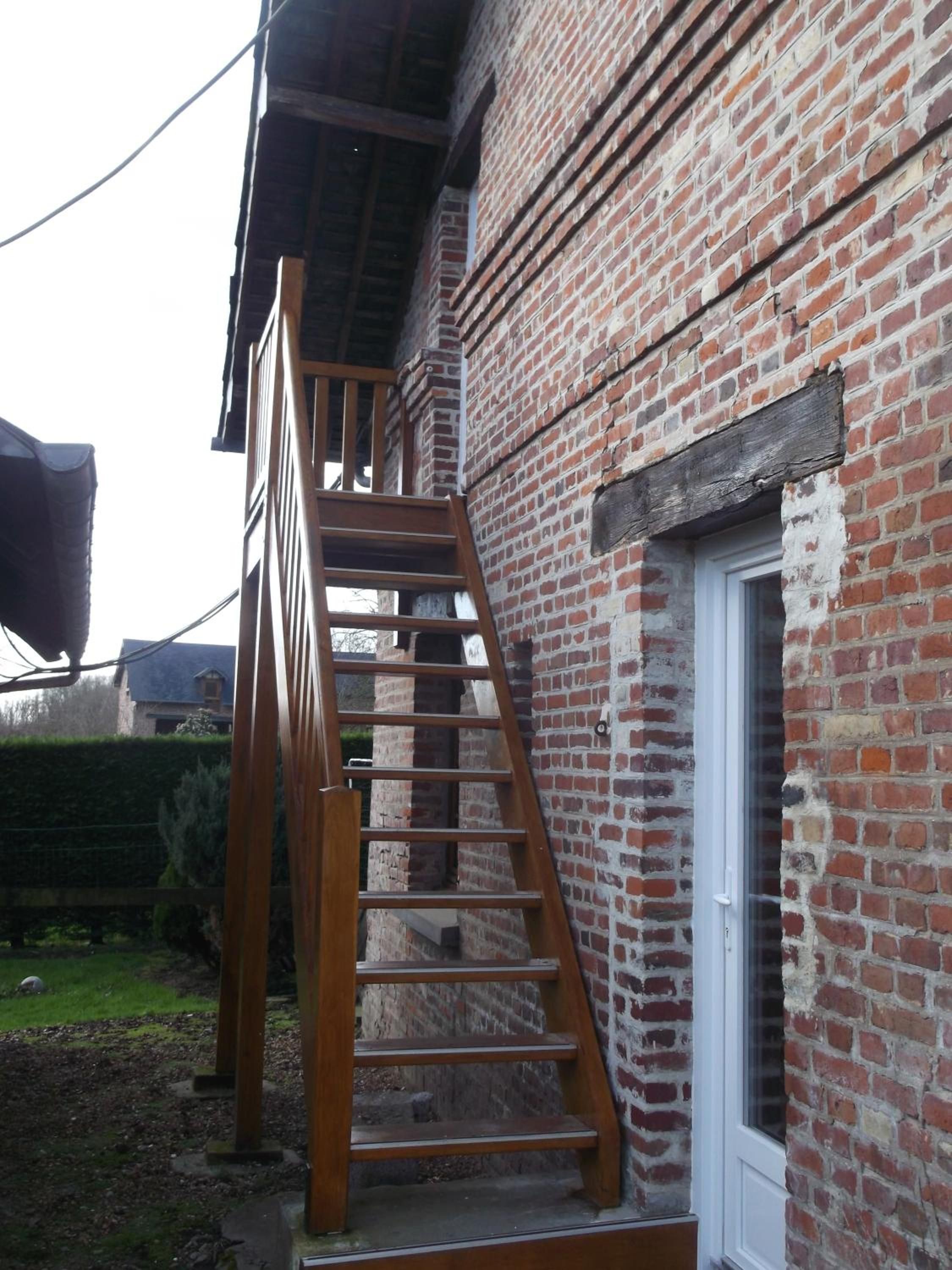 Una escalera de madera que lleva a un edificio de ladrillo con una puerta blanca.