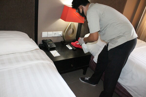 A hotel room with two beds, a desk with a telephone, a lamp, and a notepad.
