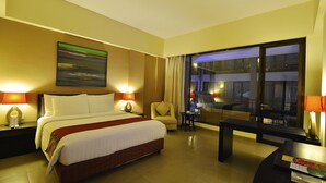 Habitación de hotel con una cama grande, un escritorio, una silla y vistas de la ciudad de noche.