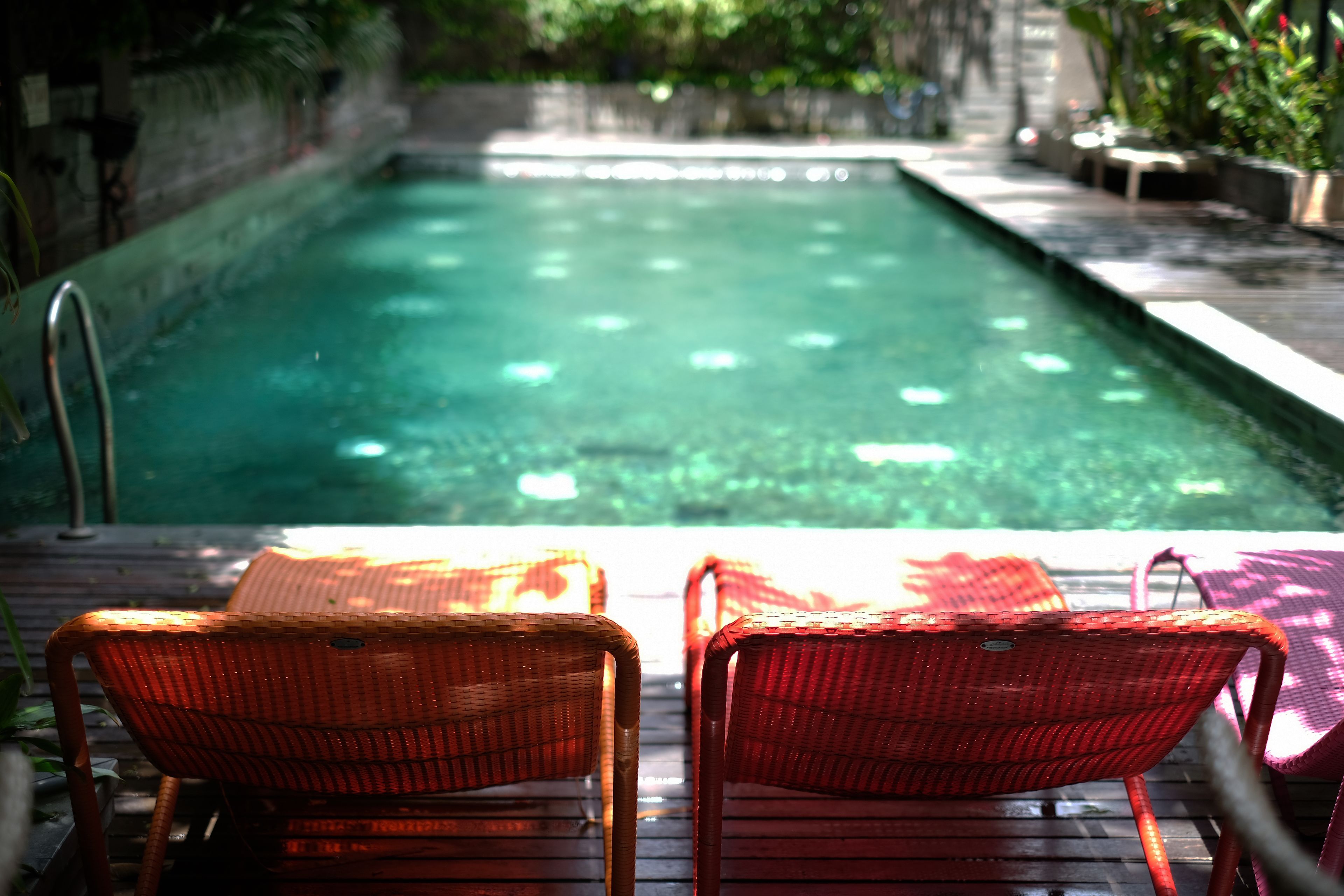 A swimming pool with two wicker lounge chairs facing the water.