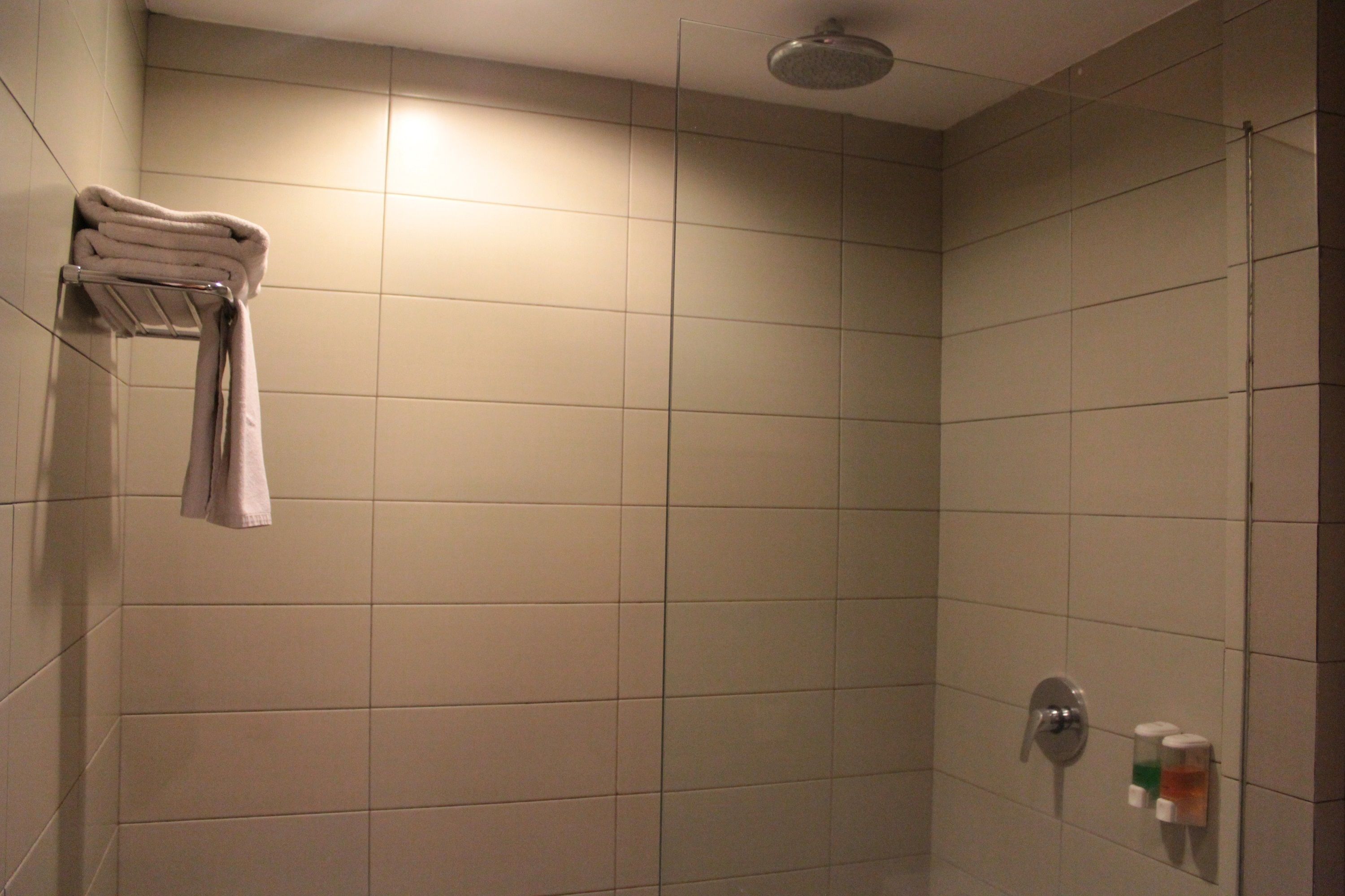 A tiled shower area with a towel rack and a hand soap dispenser.